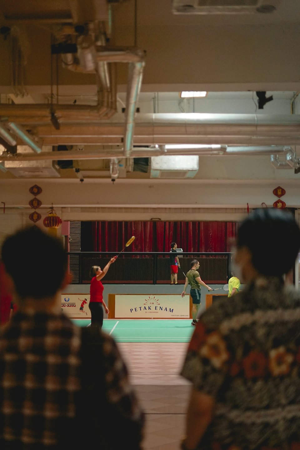 Ľudia hrajúci bedminton vo veľkej športovej hale.